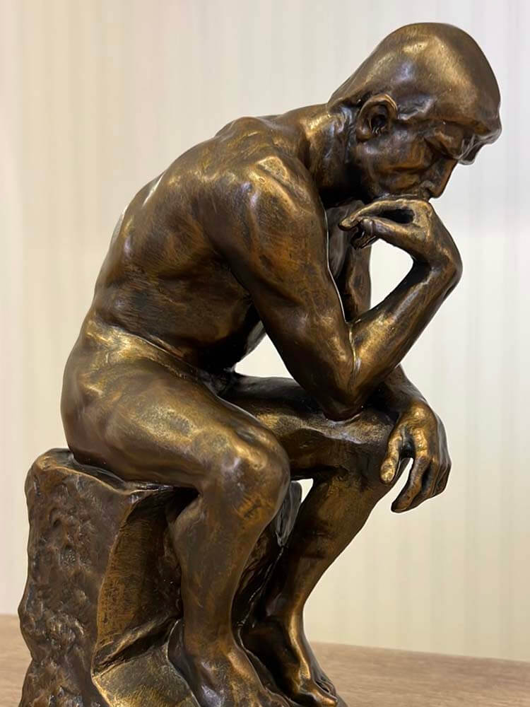 Bronze sculpture of a thinker sitting on a rock  