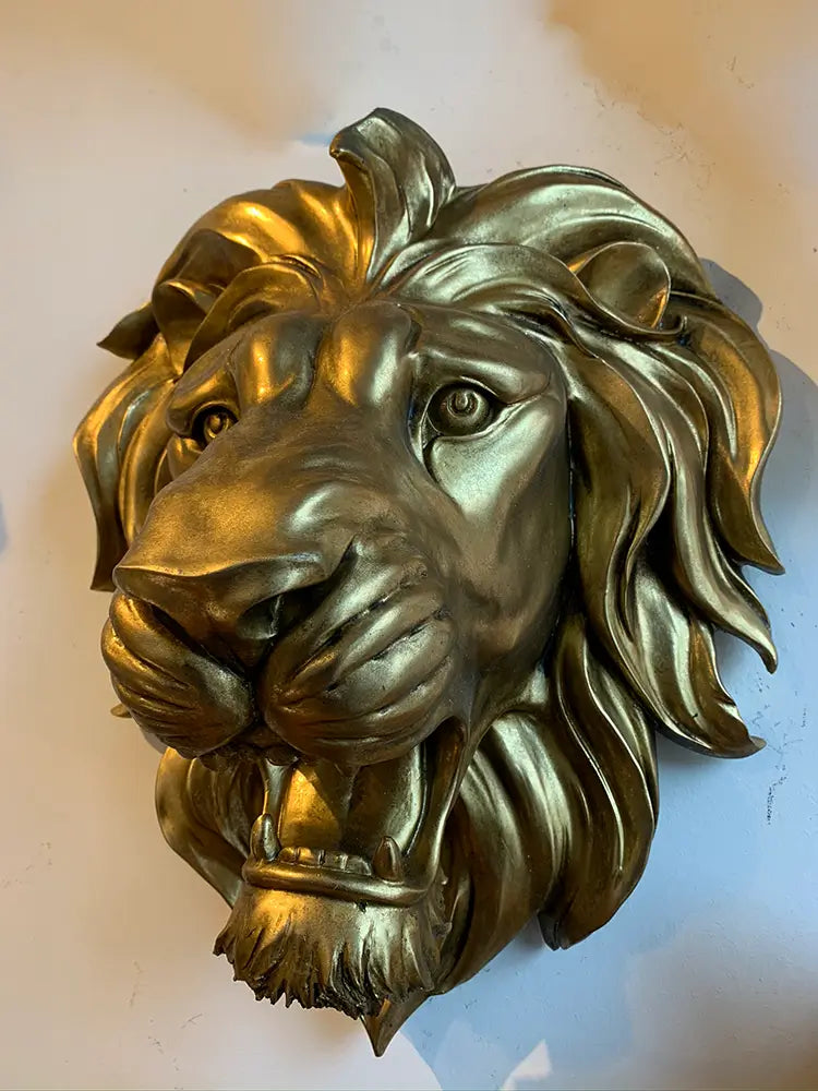 A metallic gold lion head wall sculpture, Large Lion Mane and roaring expression. Statement lion head wall mount in gold, styled on a dark moody feature wall in a modern luxury living room.
